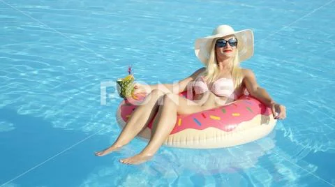 CLOSE UP: Attractive female lying on doughnut floatie drinking pineapple juice Stock Photos
