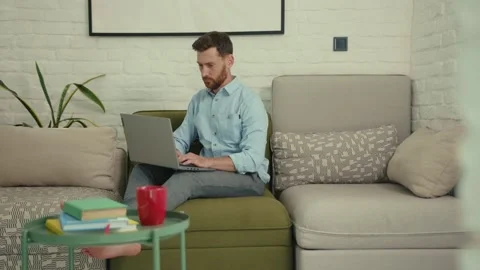 Close up attractive man using laptop typing working look around sitting on couch Stock Footage 132539663