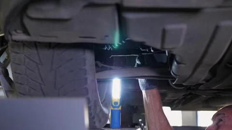 Close-up of an auto mechanic working under a car on a car lift in the garage. Stock Footage 339787483