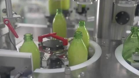 Close-up of automatic bottling machine filling green fruit juice and capping Stock Footage 334274941
