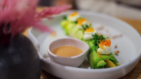 Close up of an avocado roll with sauce on a white plate at a restaurant Stock Footage 304320194