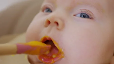 Close up of a baby being fed with a spoon, showing facial details and soft Stock Footage 329403154