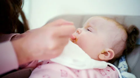 Close up of a baby being gently fed with a spoon by an adult Stock Footage 329390354