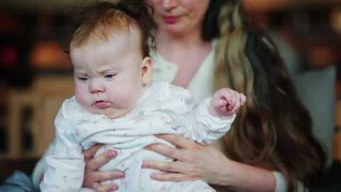 Close up of a baby being gently held by an adult indoors, with soft natural Stockbeeldmateriaal 335479375