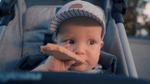 Close-up: baby eating bread while sitting in a stroller outside on a summer day Stock Footage 110858978