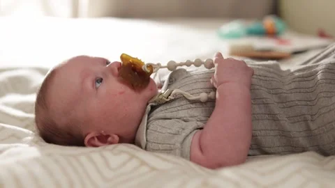 Close-up of a baby lying down with a pacifier in its mouth and a beaded clip Vidéo 340629898