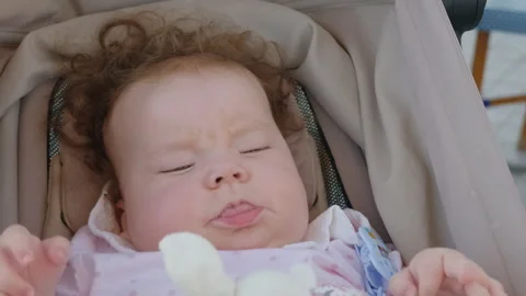 Close-up of a baby resting in a stroller, wearing a pink polka-dot outfit Vidéo 344798901