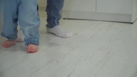 Close-up of the baby's bare feet walking on the apartment floor. Mom teaches her Stock Footage 302832950