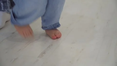 Close-up of the baby's bare feet walking on the apartment floor. Mom teaches her Stock Footage 320290738