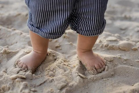 Close-up of a baby's feet sinking into soft beach sand on a sunny day Stock Photos