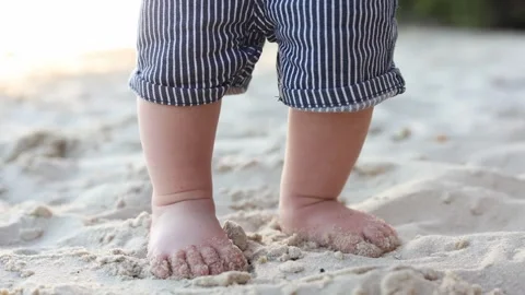 Close-up of a baby's feet walking on a sandy beach during golden hour Stock Footage 345365639