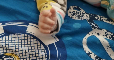 Close-up baby’s hand, lying on sofa, blue coverlet, hesitantly tries to move Stock Footage 124294634