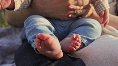 Close-up of a baby's tiny feet being held by parents outdoors Vidéo 340623153