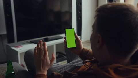 Close up back man use phone with green screen sitting sofa drink beer talk in Stock Footage 105203973