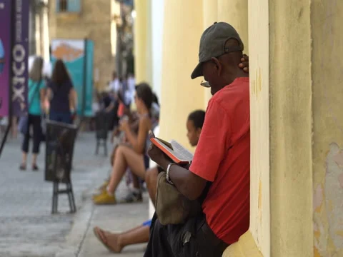 Close-up back view Afro-American man dressed red t-shirt, hat, glasses sits at Vídeos de archivo 69559015