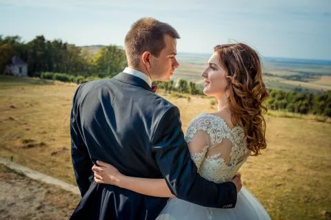 Close-up back view of the charming smiling newlyweds hugging and looking at each Stock Photos