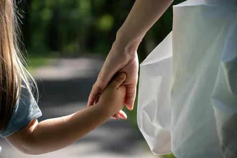 Close-up back view of a child holding mother's hand while walking in a park. Stock Photos