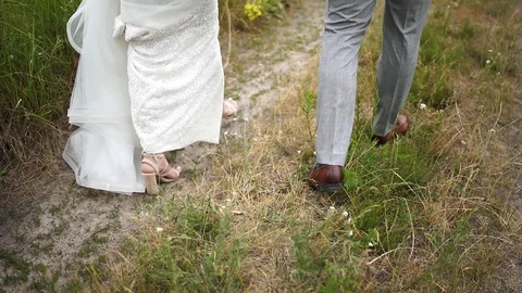 Close-up. Back view. Legs. The bride and groom are walking on the field. Stock Footage 129114551