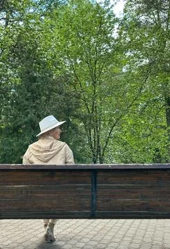 Close-up Back view A middle-aged blonde girl is sitting in a park on a benc.. Stock Photos