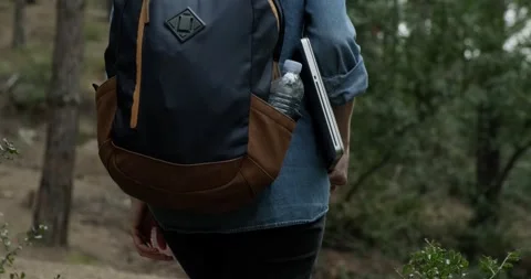 Close up back view of woman with backpack holding laptop while walking in forest Video stock 151857463