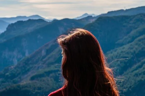 A close-up back view of a young redhead woman in front of the mountain valley Stock Photos