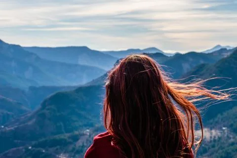 A close-up back view of a young redhead woman with her long hair fluttering i Stock Photos