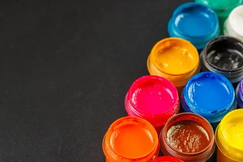 Close-up background of opened small gouache paint jars on black surface Foto stock