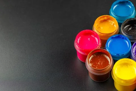 Close-up background of opened small gouache paint jars on black surface Stock Photos