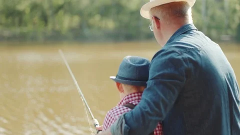 Close up backshot of little boy and his granfather in straw hats fishing Stock Footage 78376905
