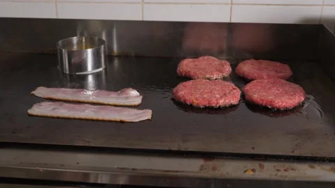 Close-up of bacon and burger patties fried on a stove in the restaurant kitchen. Stock Footage 288334781