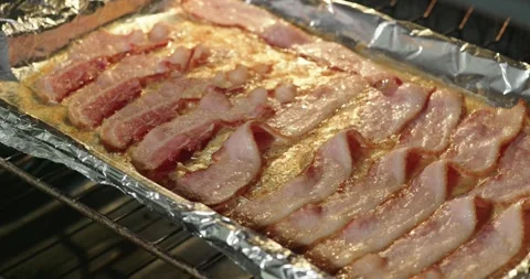 Close-Up of Bacon Rendering and Browning on Foil in a Hot Oven Stock Footage 318497491