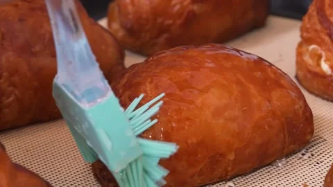 Close-up of Baker Glazing Fresh Pain au Chocolat Pastry with a Brush Stock Footage 337751429