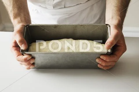 Close up of a baker holding a baking tin filled with bread dough. Stock Photos