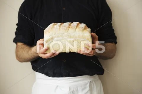Close up of a baker holding a freshly baked loaf of white bread. Stock Photos