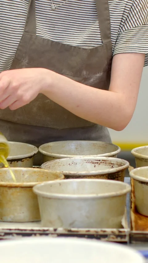 Close-up of baker pouring oil into multiple stained ramekins on prep counter Vidéo 344575483