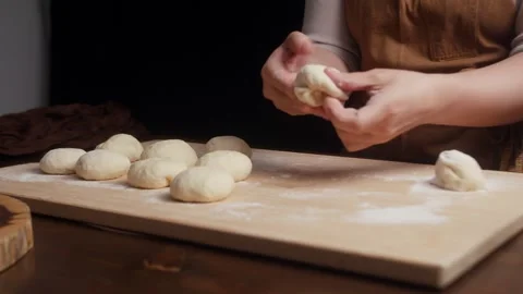 Close up of baker shaping soft dough into smooth balls by hand on a floured Vidéo 340003803