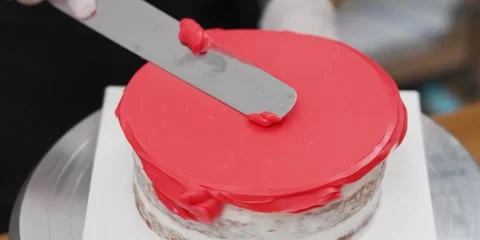 Close-Up of Baker Smoothing Vibrant Red Frosting on Top of Cake with Spatula 動画素材 343588425