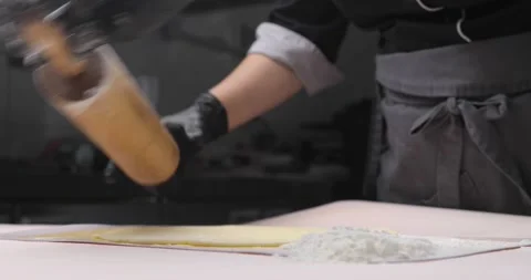 Close-up of a baker's or chef's hand rolling out dough on a white table, with Video stock 165806326