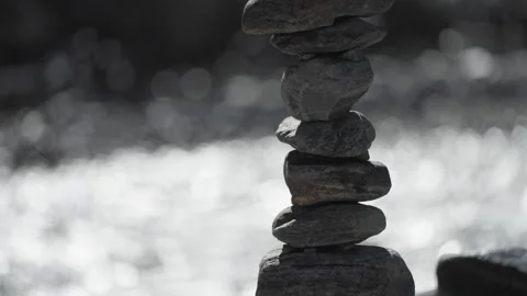 Close-up of balanced stone piles by a tranquil riverside, emphasizing Stock Footage 280477213