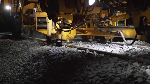 Close up of ballast and tamping machine working on track maintenance at night Stock Footage 328989949