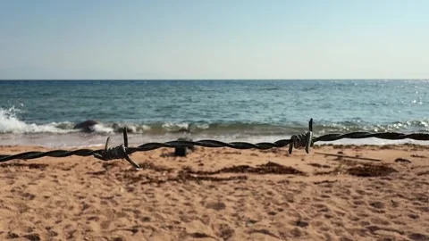Close Up of Barbed Wire Fence on Sandy Beach with Turquoise Sea in Background Stock Footage 333247042