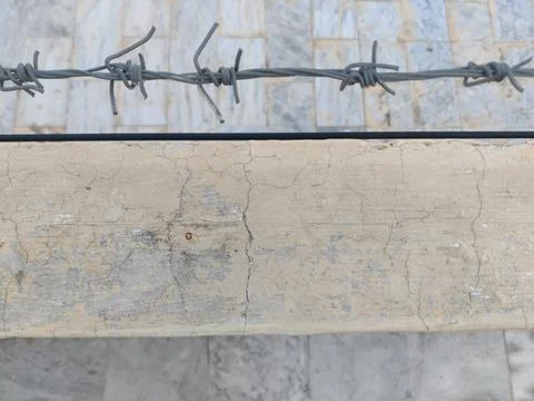 Close up of barbed wire over a concrete wall with cracked and aged paint Stock Photos