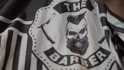 Close-up of a barber cape with a skull logo, scissors, and a straight Stock Footage 283526328