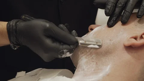 Close-up of a barber's hand while shaving a client's cheeck with a razor Vídeo Stock 116886505