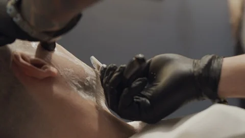 Close-up of a barber's hand while shaving a client's cheeck with a razor Stock Footage 116886712