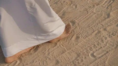 Close-up of the bare feet of a man in white long clothing. Walking in the sand. Stock Footage 105674603