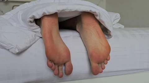 Close-up of bare feet under a white blanket on a bed. Bare feet sticking out Video stock 282103592