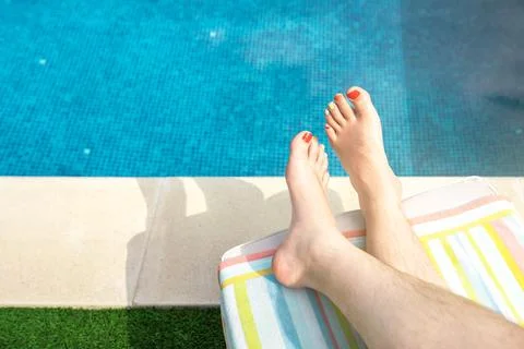 Close-up of the bare feet of a young man lying on a deckchair in a swimming pool Stock Photos