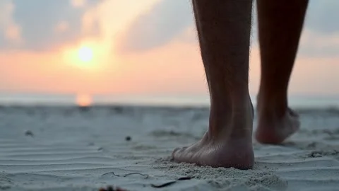 Close-up of the bare feet of a young men walking barefoot on a sandy beach by Stock Footage 242559299