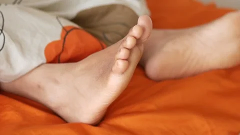 Close up of bare human feet moving under blanket on orange bed sheet in bed.. Stock-Footage 332578945